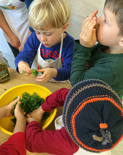 Kids making kale salad by massaging in olive oil via LizsHealthyTable.com