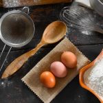 Kitchen utensils and food at the old home kitchen table. Chicken eggs and wheat flour for the dough preparation. Rustic style. Top view close-up.